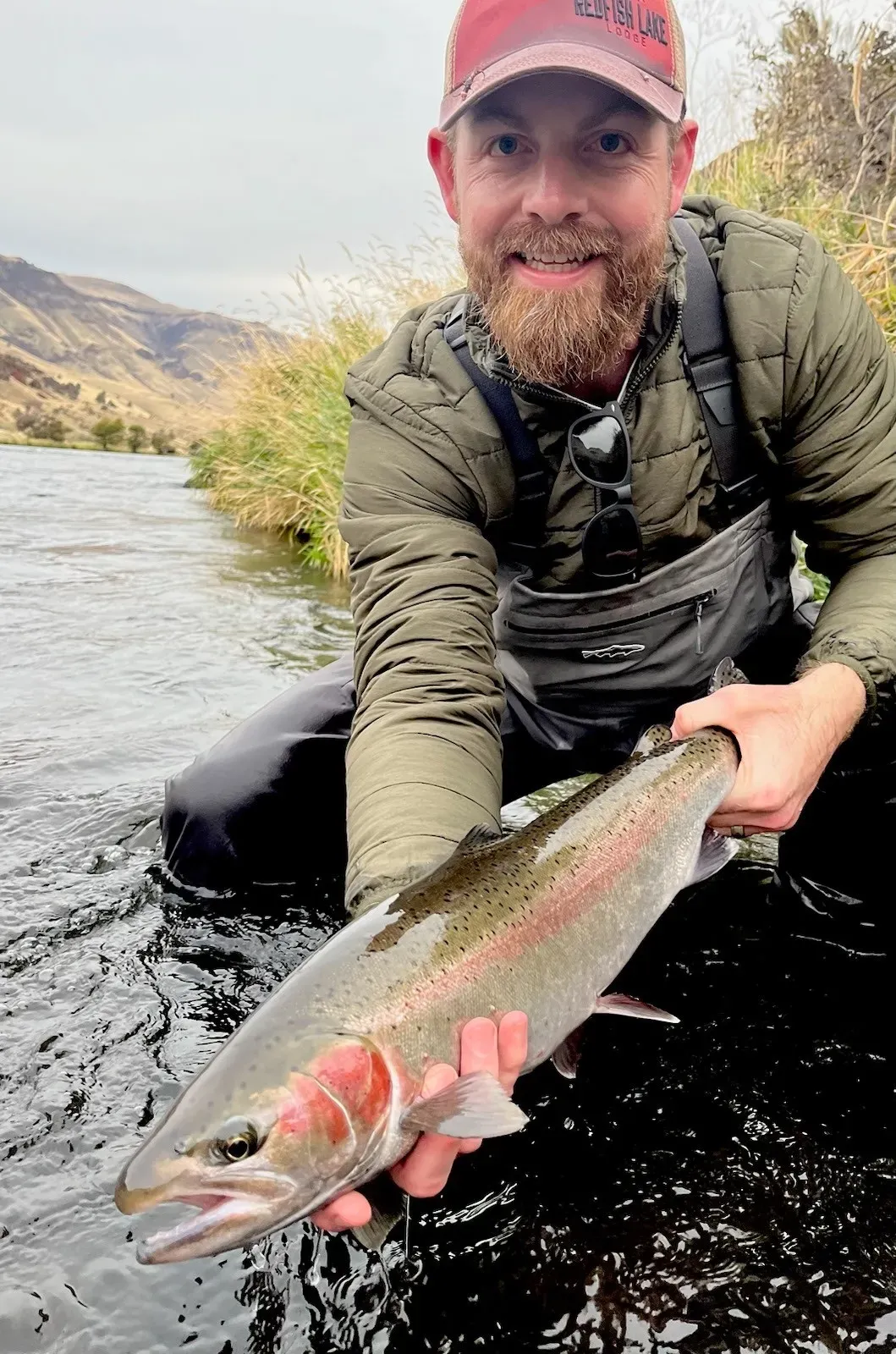 Derrick kneeling in a river, holding a steelhead