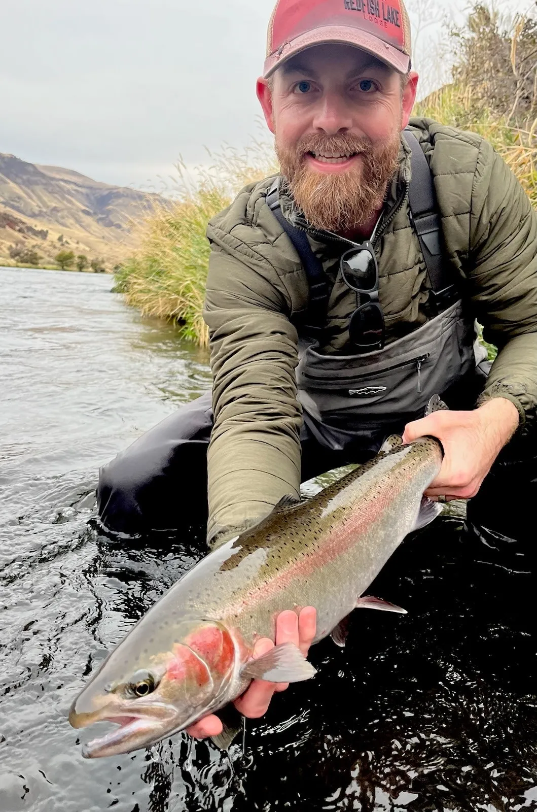 Derrick kneeling in a river, holding a steelhead